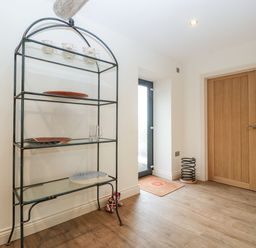 A hallway with a metal shelf holding plates and mugs next to a glass door and wooden door at Palace Farmhouse in St Weonards