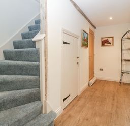 A hallway with carpeted stairs small door paintings on walls and a metal shelving unit at Palace Farmhouse in St Weonards