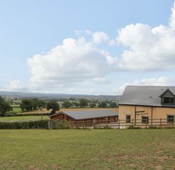A rural landscape with a yellow building and wooden structure surrounded by fields at Palace Farmhouse in St Weonards