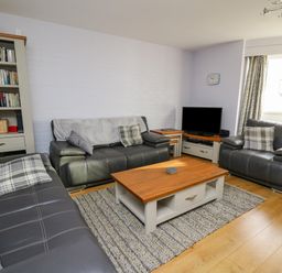 A living room with three leather sofas a wooden coffee table a bookshelf and a television at 1 St Marys Court in Tenby