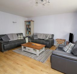 A living room with grey leather sofas a wooden coffee table a rug a bookcase and a television at 1 St Marys Court Tenby