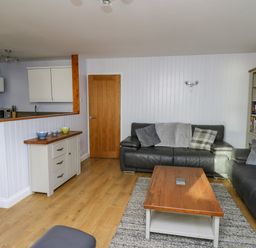 A living room with black leather sofas wooden coffee table and a kitchen area at 1 St Marys Court in Tenby