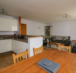 An open plan kitchen and living area with wooden dining table and chairs white kitchen cabinets grey sofas and a bookshelf at 1 St Marys Court in Tenby