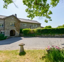 A two-story building with an arched entrance surrounded by greenery and a driveway at Twelve Oaks Farmhouse in Teigngrace near Newton Abbot