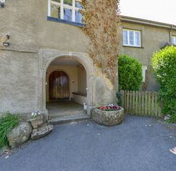 Arched stone entrance with wooden door and flower pots in front of a stone building with windows and ivy at Twelve Oaks Farmhouse in Teigngrace near Newton Abbot