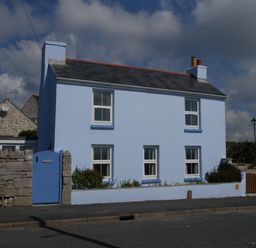 A blue two story house with white framed windows and a stone wall in front at Fisherman's Cottage in Southwell