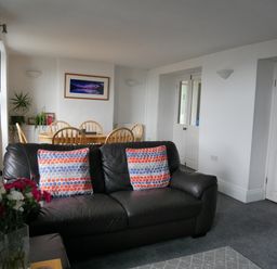 A living room with a black leather sofa and dining table with wooden chairs at Fisherman's Cottage in Southwell