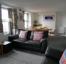 A living room with black leather sofas and a wooden dining table with chairs at Fisherman s Cottage in Southwell