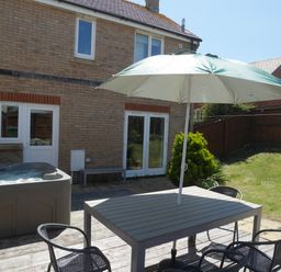 A backyard with a hot tub patio table chairs and umbrella at Cliffwalk Cottage in Southwell
