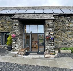 Stone barn with glass door entrance flowers in pots and solar panels on roof at Meadow Syke Barn in Bampton Cumbria