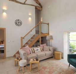 A living room with a beige sofa, green armchair, small wooden tables, stairs with wooden railing and glass panels at Meadow Syke Barn in Bampton Cumbria