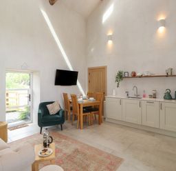 A kitchen and dining area with wooden dining table and chairs a green armchair a sofa and a wall mounted TV at Meadow Syke Barn in Bampton Cumbria