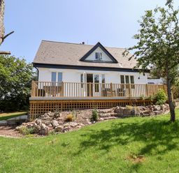 A house with a wooden deck and garden with rocks and trees at Melbecks in Abergele