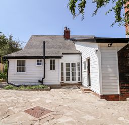 An exterior view of a white house with a stone patio and surrounding trees at Melbecks in Abergele