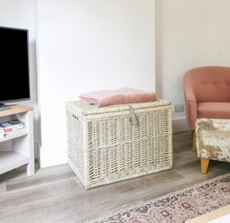 A room with a television on a stand a wicker basket with a blanket a pink armchair and a patterned rug at River Lym Cottage in Lyme Regis