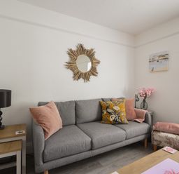 A living room with a gray sofa pillows a side table lamp and wall mirror at River Lym Cottage in Lyme Regis