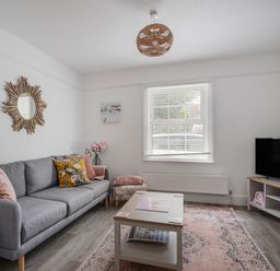 A living room with a gray sofa a coffee table a television and a window at River Lym Cottage in Lyme Regis