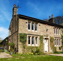 A stone house with multiple windows ivy growing on the walls a white door and a garden with flowers at The Lodge in Hartlington near Grassington