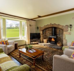 A living room with a wood-burning stove fireplace a wooden coffee table and armchairs at The Lodge in Hartlington near Grassington