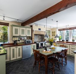 A kitchen with a wooden dining table and chairs a stove and cabinets with windows showing outside at The Lodge in Hartlington near Grassington