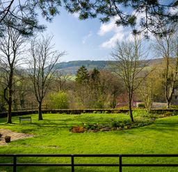 A garden with grass trees a bench and distant hills at Kail House in Grassington