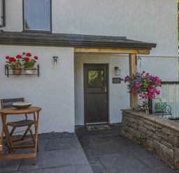 An outdoor patio with a wooden table and chairs flower pots on the wall and a door at How Hill Farm Cottage in Greystoke
