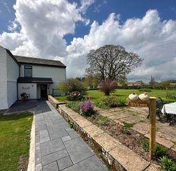 An outdoor area with a house, pathway, and welcome sign at How Hill Farm Cottage in Greystoke