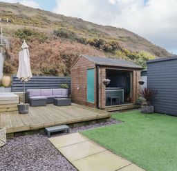 An outdoor patio with a wooden deck sofa set umbrella shed and artificial grass at The Chalet in Coulderton near Egremont Cumbria