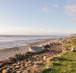A rocky beach with waves and grass next to a pathway made of large rounded stones at The Chalet in Coulderton near Egremont Cumbria