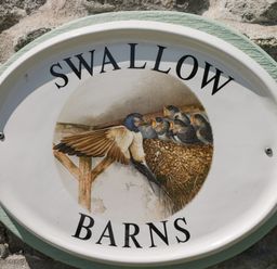 An oval sign on a stone wall with birds and nest illustration and text swallow barns