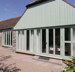 Exterior of a stone building with multiple light green framed glass doors and windows at Swallow Barns in Chipping Sodbury