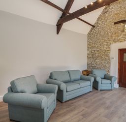 A living room with blue sofa and chairs wooden floor stone wall with door and exposed ceiling beams at Swallow Barns in Chipping Sodbury