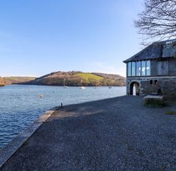 A waterfront area with a stone building and boats on the water at Oakenhurst in Golant