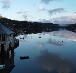 A body of water with small boats and a stone building on the shore at Oakenhurst in Golant