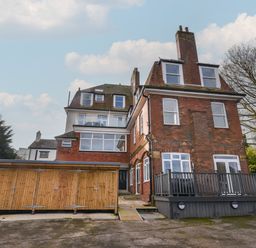 A large brick and white multi-story house with multiple windows and a wooden shed at The Bungalow in Lyme Regis
