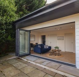 An outdoor patio area with stone tiles adjacent to a living room with a blue sofa and nested coffee tables at The Bungalow in Lyme Regis