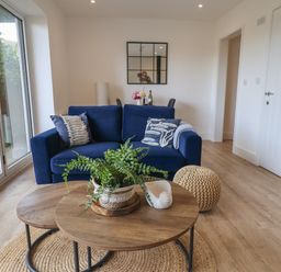 A living room with a blue sofa cushions coffee tables and a woven pouf at The Bungalow in Lyme Regis