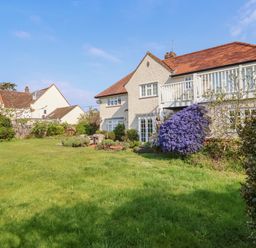 A large garden with lawn chairs and flowering bushes outside a two-story house with a balcony at Halsey in Walberswick