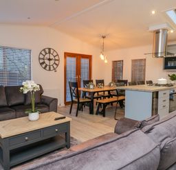 A living area with sofas and a coffee table next to a dining table and a kitchen at 25 Thirlmere in Troutbeck Bridge
