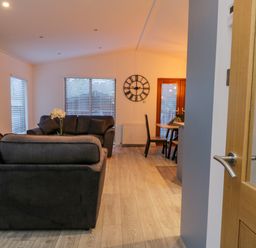 A living area with two dark sofas a wall mounted television a clock and a dining table with chairs at 25 Thirlmere in Troutbeck Bridge