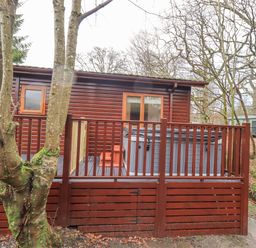 A wooden cabin with a fenced porch and trees around at 25 Thirlmere in Troutbeck Bridge