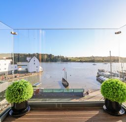 A balcony with two potted plants overlooking a river with boats and buildings at The Penthouse in Woodbridge