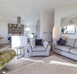 A living room with grey sofas and a green armchair next to a kitchen area at The Penthouse in Woodbridge