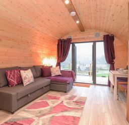A wooden room with a gray sofa and purple cushions and curtains at Lovies Place - Crossgate Luxury Glamping in Hartsop near Glenridding