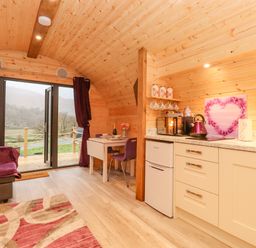 A wooden cabin interior with a small kitchen area a dining table with chairs and a sofa near glass doors at Lovies Place - Crossgate Luxury Glamping in Hartsop near Glenridding