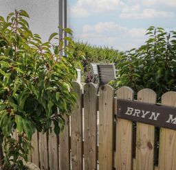 A wooden fence with a Bryn Mor sign and green plants behind it at Bryn Mor in Benllech