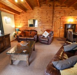 A living room with brown leather sofas a coffee table wooden walls and a dining table at Avocet Lodge in Tattershall Lakes Country Park