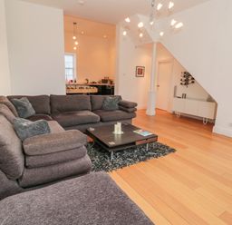 A living room with a sectional sofa and coffee table on a rug and a kitchen area in the background at 2 The Reformed Church in Embleton