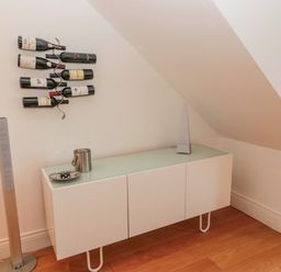 A white cabinet with items on top and wine bottles mounted on the wall in a room with wooden floor at 2 The Reformed Church in Embleton