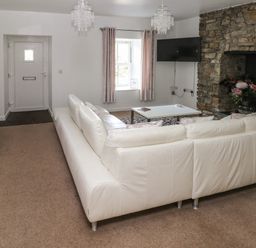 A living room with a white sofa stone fireplace and a wall mounted TV at The Old Farm House in Redberth near Pentlepoir